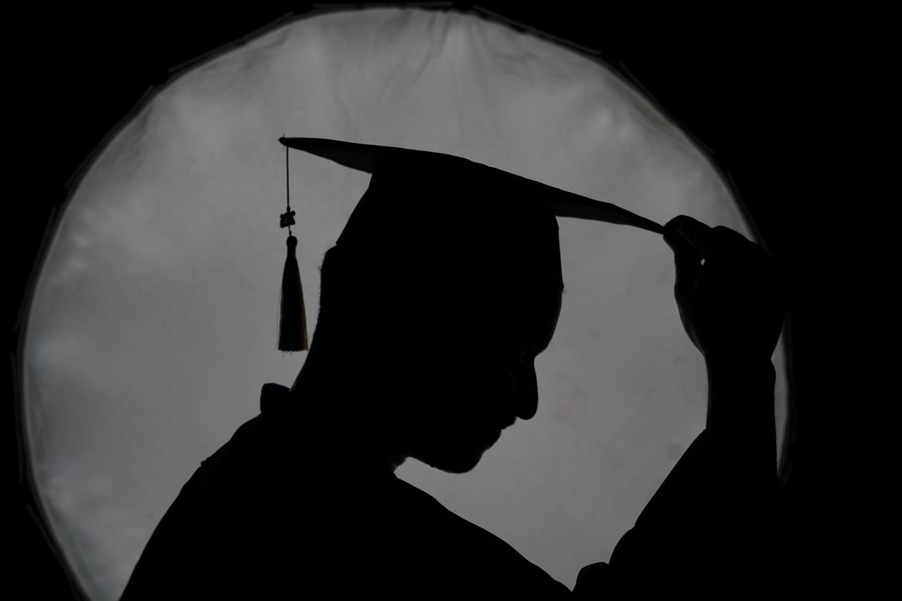 Mastering the First Impression: Your intriguing post title goes here Silhouette of a graduate adjusting their cap against a diffused light backdrop, conveying accomplishment.